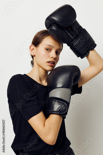 young woman in boxing gloves in black pants and a T-shirt light background