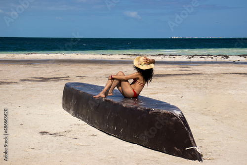 sexy woman sunbathing in bikini on top of a boat on a caribbean sea beach while looking at the ocean horizon.