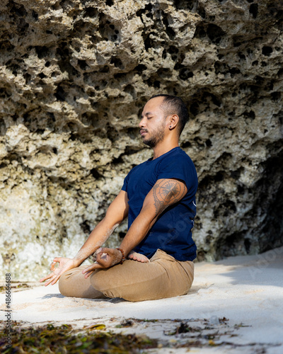 Meditation and yoga on the beach. Asian man sitting on the sand in Lotus pose. Padmasana. Hands in gyan mudra. Closed eyes. Yoga retreat. Healthy lifestyle. Thomas beach  Bali