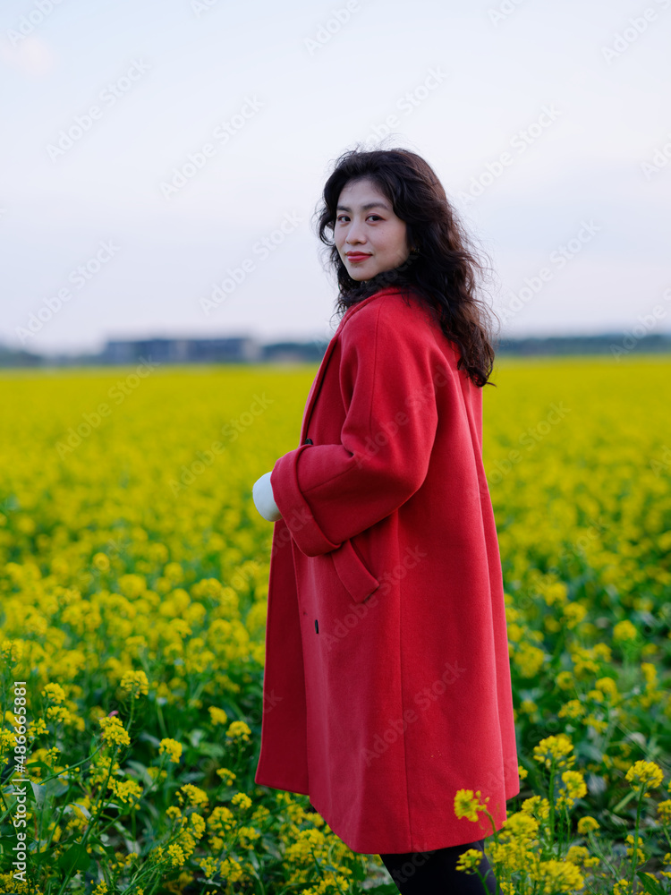 An Asian woman in a red trench coat stands in a field of rape flowers An Asian woman in a red trench coat stands in a field of rape flowers