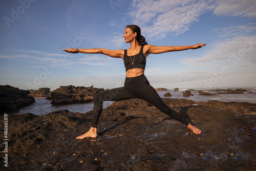 Slim Asian woman practicing of Virabhadrasana II. Warrior II Pose. Yoga retreat. Healthcare concept. Balance and concentration. Strong fit body. Copy space. Mengening beach, Bali