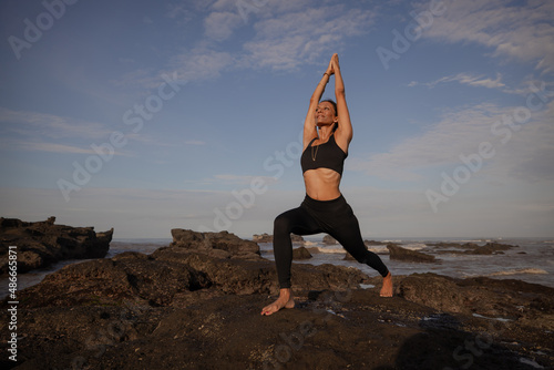 Asian woman practicing Virabhadrasana I, Warrior I Pose. Hands raised up in namaste mudra. Yoga retreat. Healthcare concept. Balance and concentration. Copy space. Mengening beach, Bali