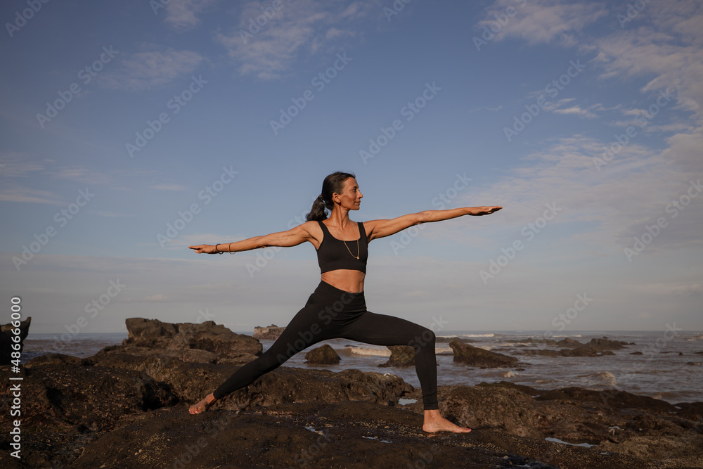 Slim Asian woman practicing Virabhadrasana II, Warrior II Pose. Yoga retreat. Healthcare concept. Balance and concentration. Zen life. Strong fit body. Copy space. Mengening beach, Bali Slim Asian woman practicing Virabhadrasana II, Warrior II Pose. Yoga retreat. Healthcare concept. Balance and concentration. Zen life. Strong fit body. Copy space. Mengening beach, Bali