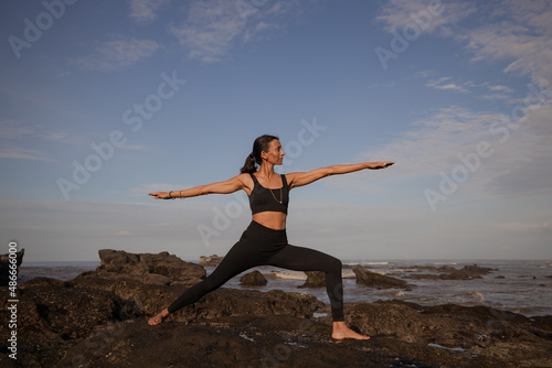Slim Asian woman practicing Virabhadrasana II, Warrior II Pose. Yoga retreat. Healthcare concept. Balance and concentration. Zen life. Strong fit body. Copy space. Mengening beach, Bali