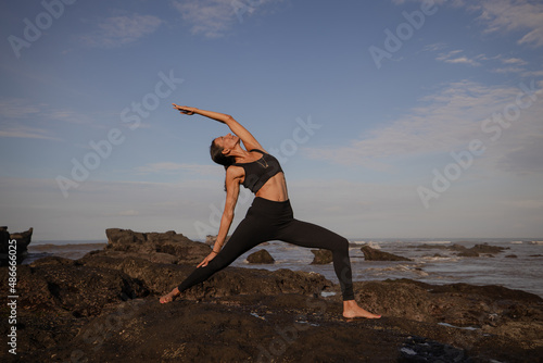 Slim Asian woman practicing variation of Virabhadrasana I. Warrior I Pose. Yoga retreat. Healthcare concept. Balance and concentration. Strong fit body. Copy space. Mengening beach, Bali