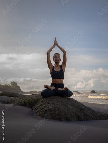 Meditation yoga on the beach. Asian woman sitting on the rock in Lotus pose. Padmasana. Hands raised up in namaste mudra. Yoga retreat. Healthy concept. Copy space. Mengening beach  Bali