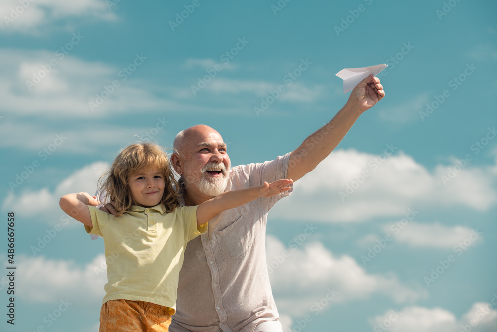 Grandfather and grandson playing with paper plane against summer sky background. Child boy with dreams of flying or traveling. Grandfather and grandson playing with paper plane against summer sky background. Child boy with dreams of flying or traveling.