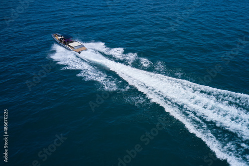 Boat drone view. Dark gray blue boat in motion at sea. Speedboat moving fast on blue water aerial view.