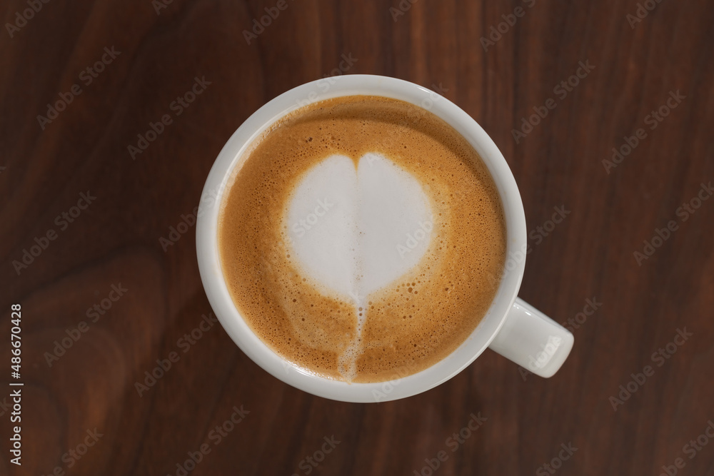 Fototapeta premium Flat white in white cup with simple latte art on walnut wood table