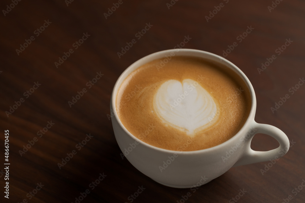 Flat white in white cup with simple latte art on walnut wood table Flat white in white cup with simple latte art on walnut wood table