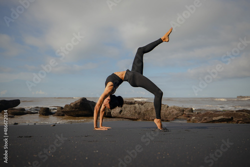 Bali yoga. Slim Asian woman practicing Eka Pada Chakrasana, One Legged Wheel Pose. Upward facing bow pose is a deep backbend. Straight leg. Copy space. Yoga retreat. Mengening beach, Bali