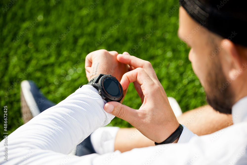 a white man in black shorts and a white shirt looks at a sports watch and adjusts it a white man in black shorts and a white shirt looks at a sports watch and adjusts it