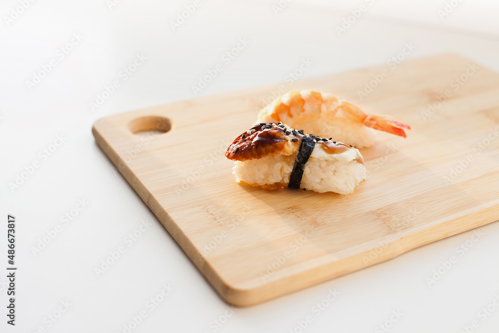 Sushi delivery and takeout - Nigiri and unagi sushi japanese food on wooden board isolated on white. Nigiri unagi sushi and chopsticks japanese food on wooden board close up. Sushi delivery and takeout - Nigiri and unagi sushi japanese food on wooden board isolated on white. Nigiri unagi sushi and chopsticks japanese food on wooden board close up.