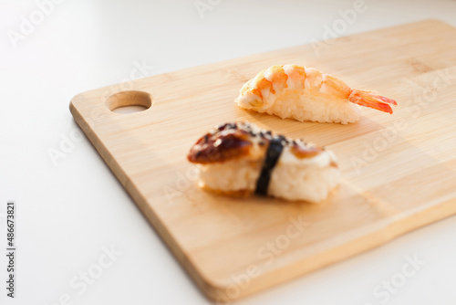 Sushi delivery and takeout - Nigiri and unagi sushi japanese food on wooden board isolated on white. Nigiri unagi sushi and chopsticks japanese food on wooden board close up.