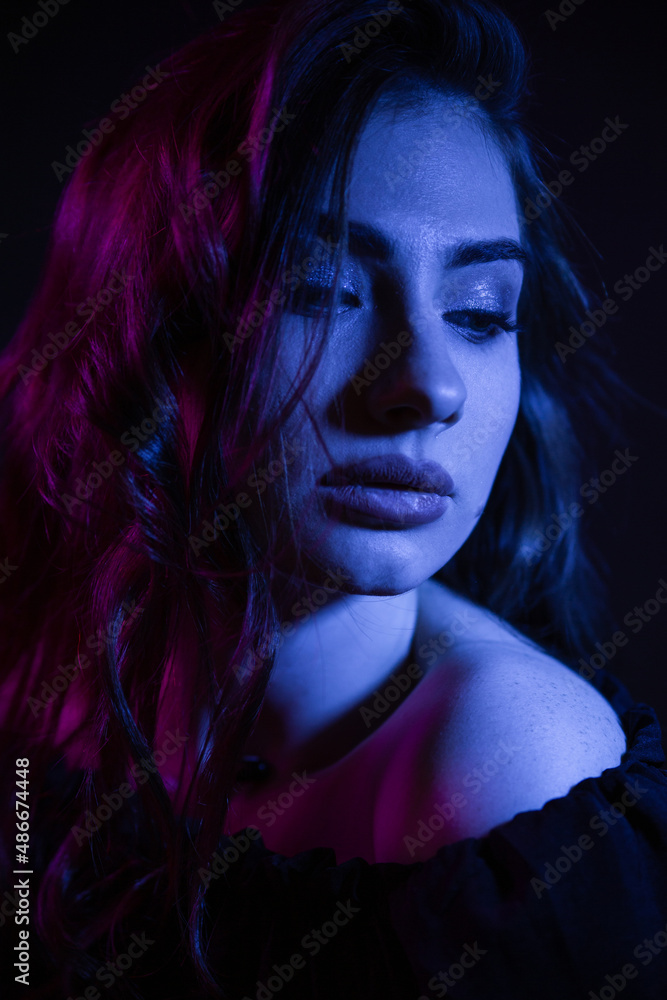 Young woman in the dark in a club. Girl in blue and pink.