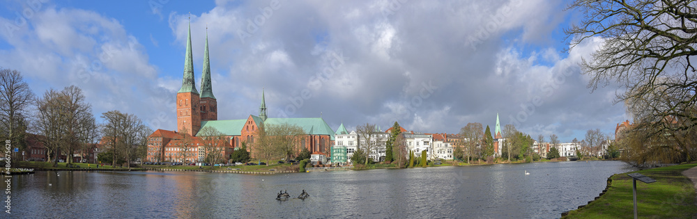 City panorama of the historical old town Lubeck with the Dom, a two-towered gothic cathedral in red brick architecture, seen from the mill pond, cloudy blue sky on a sunny day, copy space
