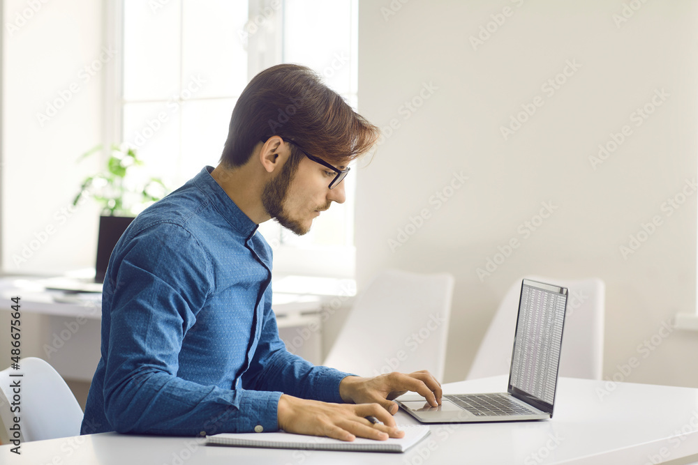 Focused millennial Caucasian man sit at desk work online on computer make notes write. Young successful businessman look at laptop screen study on web take training or course. Education concept. Focused millennial Caucasian man sit at desk work online on computer make notes write. Young successful businessman look at laptop screen study on web take training or course. Education concept.