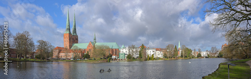 City panorama of the historical old town Lubeck with the Dom, a two-towered gothic cathedral in red brick architecture, seen from the mill pond, cloudy blue sky on a sunny day, copy space