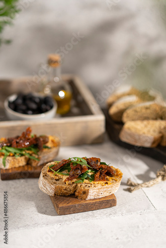 Ciabatta bread sandwich with humus and dried tomatoes, arugula leaves on white table. Italian traditional food - bruschetta, antipasto. with ingredients. Copy space. 