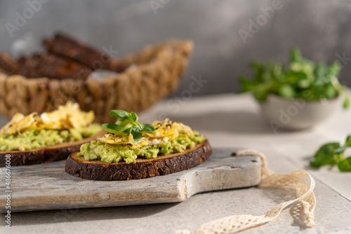 Avocado and egg sandwich with whole grain brown bread and greens, healthy diet vegan food. Breakfast on wooden board, white table. Copy space.