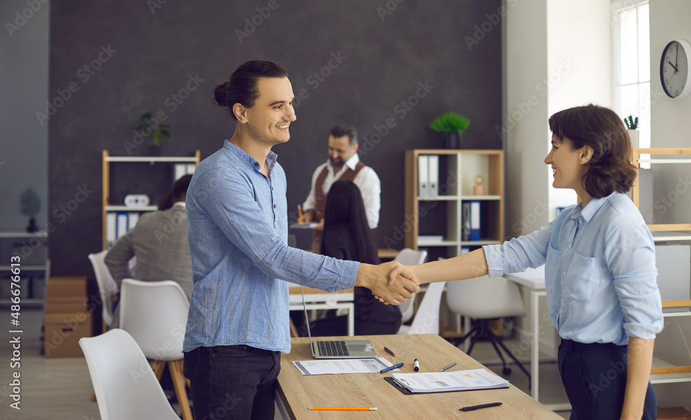 Man and woman handshake in office after job recruitment meeting. Young newcomer and millennial businesswoman HR manager shake hands to seal deal greeting or thanking each other while having interview Man and woman handshake in office after job recruitment meeting. Young newcomer and millennial businesswoman HR manager shake hands to seal deal greeting or thanking each other while having interview