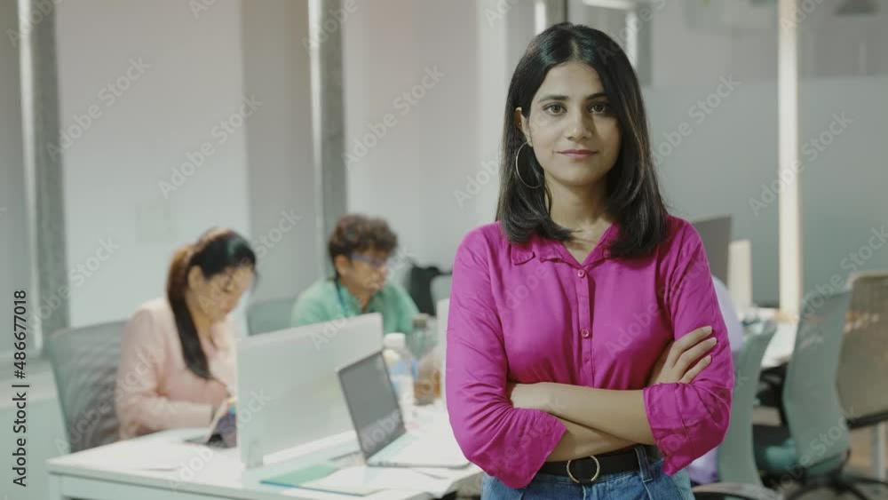 Smiling confident young Indian girl looking at camera standing at office home in apartment arms crossed.Portrait of young successful business woman standing in office. Smiling confident young Indian girl looking at camera standing at office home in apartment arms crossed.Portrait of young successful business woman standing in office.