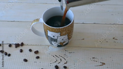 From the coffee maker, black coffee is poured into a cup, scattered coffee beans next to it.