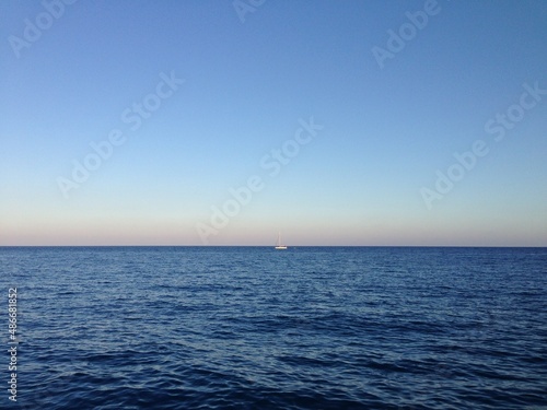 White sailboat in the high seas. White boat in the open sea. Small white sailboat on the surface of blue sea. A sailboat on the horizon in the deep blue sea © zhecka