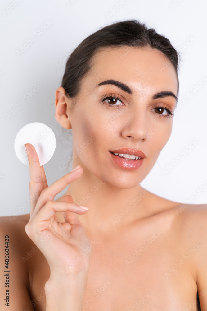 Close beauty portrait of a topless woman with perfect skin and natural makeup removing cotton pads, on a white background. Close beauty portrait of a topless woman with perfect skin and natural makeup removing cotton pads, on a white background.