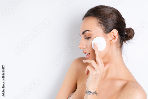Close beauty portrait of a topless woman with perfect skin and natural makeup removing cotton pads, on a white background.