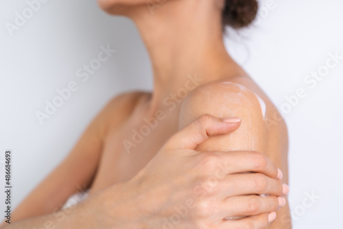 Close beauty portrait of topless woman with perfect skin holding bottle of shampoo  lotion  apply on shoulders and body  on white background