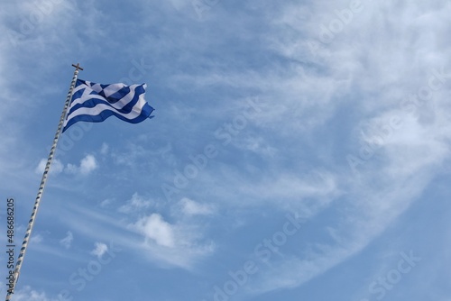 View of the greek flag waving in the air and a blue sky with a few clouds