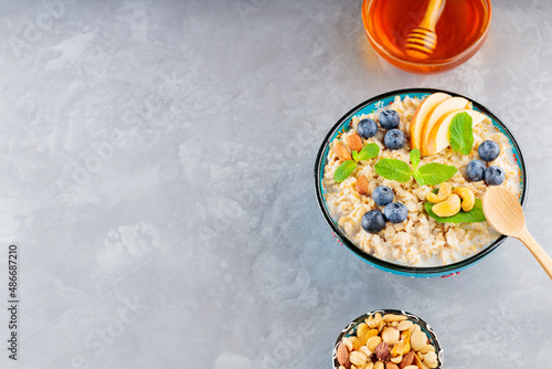 Oatmeal bowl with blueberry, nuts and honey on a gray background. Oatmeal porridge with apple and fresh mint. Healthy breakfast. Top view. Copy space