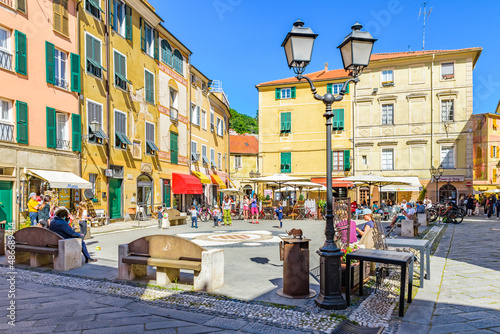 Fototapeta Naklejka Na Ścianę i Meble -  Finalborgo, Finale Ligure, Italy. May 5, 2021. View of Piazza Garibaldi with people and tourists sitting outside at the coffee tables.