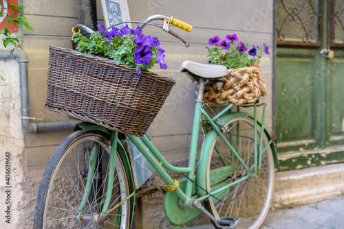 Finalborgo, Finale Ligure, Italy. May 5, 2021. In a small street in the center an old green bicycle leaning against a wall with wicker baskets with flower pots inside. photo