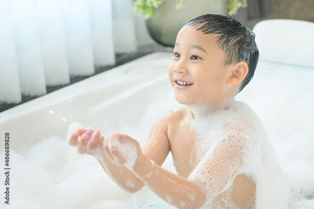 smiling happy asian child boy is playing with white foam in tub bath at home. smiling happy asian child boy is playing with white foam in tub bath at home.