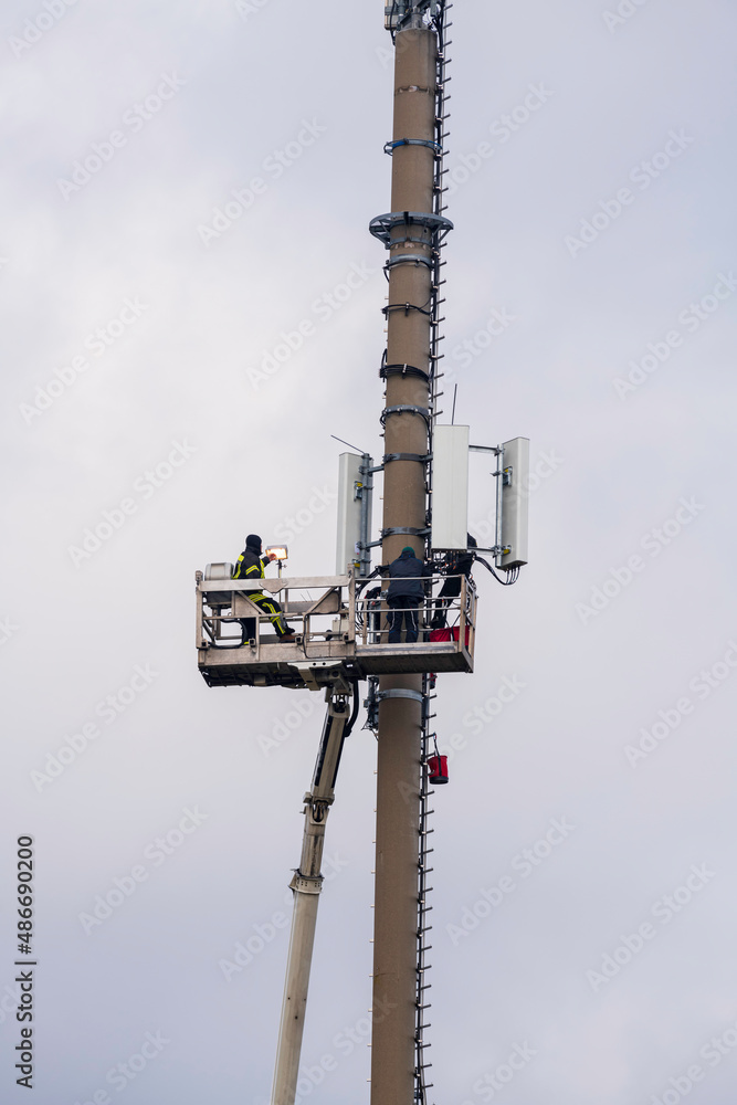 Monteure mit einem Steiger an einen Mobilfunkmast bei Wartungsarbeiten Monteure mit einem Steiger an einen Mobilfunkmast bei Wartungsarbeiten