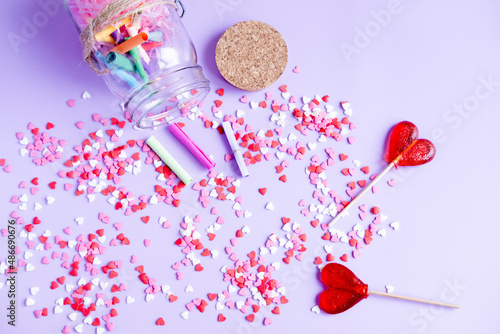heart-shaped lollipops, Small roll papers, hearts and a jar on a purple background. Jar with wishes for Valentine's Day.