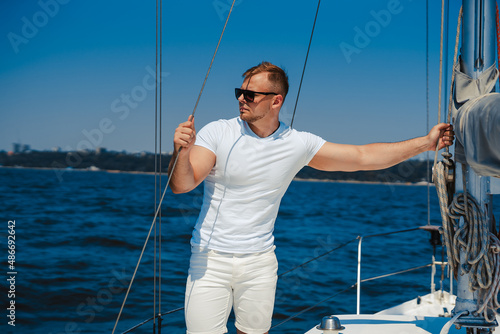 Beautiful muscular young man in white clothing enjoys walk on yacht while looking at the blue sea. Turkey 