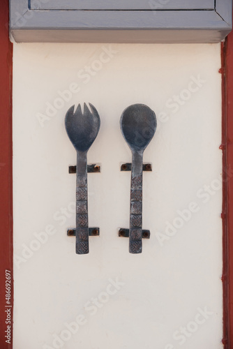 Принти на полотні Large metal and old spoon and fork with carvings and patterns on them hang on the wall of cafe or restaurant on Santorini island, Oia, Greece