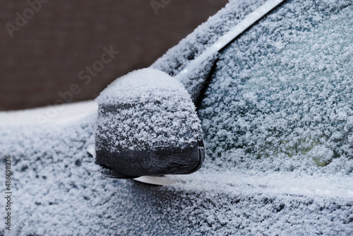 Frozen snow rearview mirror  of black car with ice and frost.Side view by close up.Selective focus.Concept of dangerous winter weather  for transport.