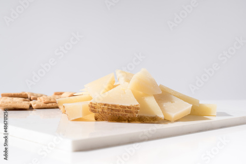 Trozos de queso manchego de oveja curado con tostadas de pan crujiente sobre una mesa blanca. Tapas españolas