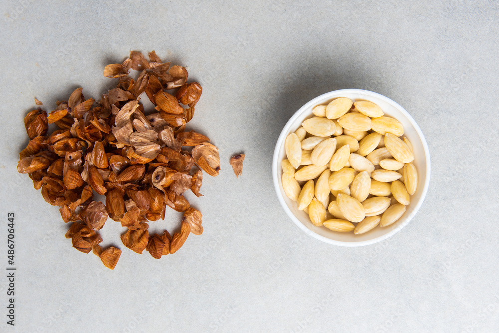 peeled almonds in a white bowl and a peel from it next to a concrete background. concept for a recipe for making almond flour. top view peeled almonds in a white bowl and a peel from it next to a concrete background. concept for a recipe for making almond flour. top view