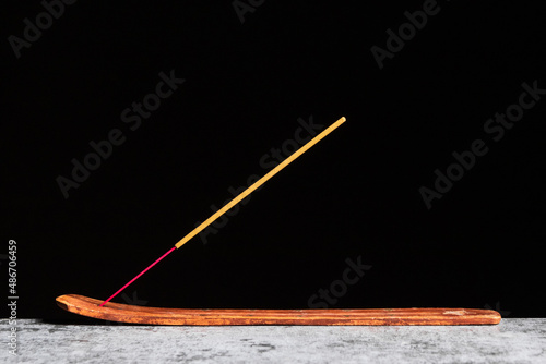 A stick of incense stands on a wooden stand isolated on a black background
