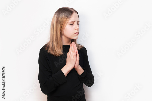 Obraz na plátně A young girl with a sad, pleading face holds her hands in front of her and prays, talks to God, to herself, her eyes closed