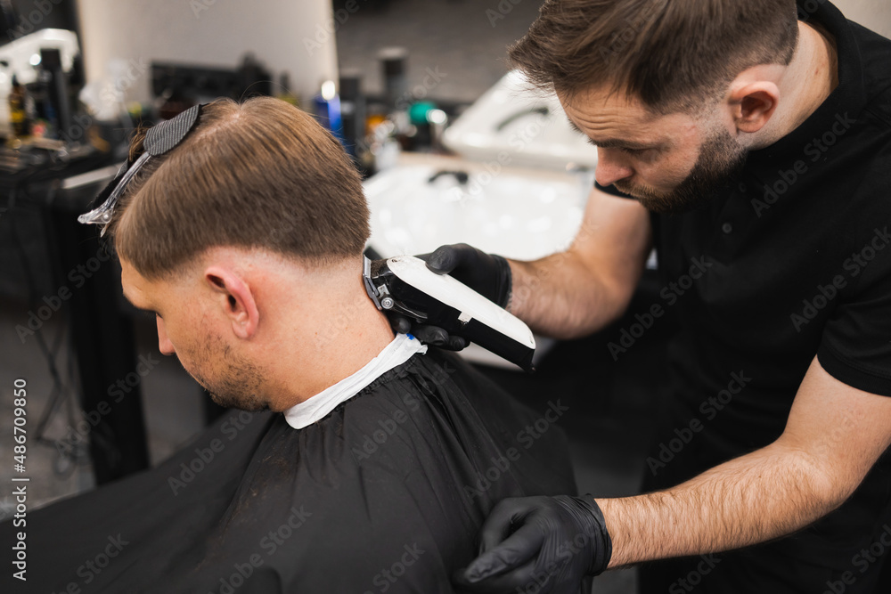 Young man in barbershop. Hairdresser cuts the hair from the back of the client's head with a electric clipper Young man in barbershop. Hairdresser cuts the hair from the back of the client's head with a electric clipper