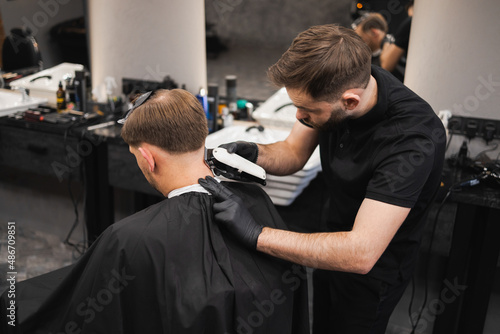 Male hairdresser making a haircut for a young man in a barber shop