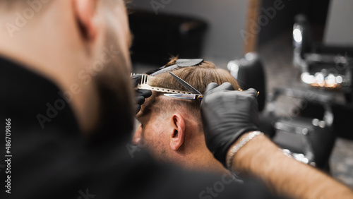 Hairdresser scissors hair on the head sides for a stylish black-haired man in the barbershop
