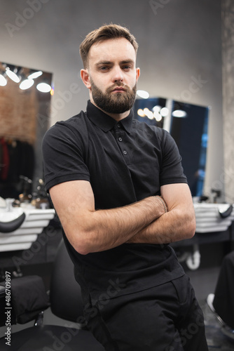 Confident male hairdresser standing with arms crossed in barbershop.
