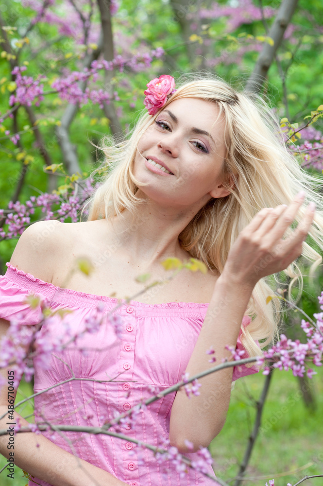 Hppy smiling healthy woman with luxury blonde hair posing in blooming sakura blooming park